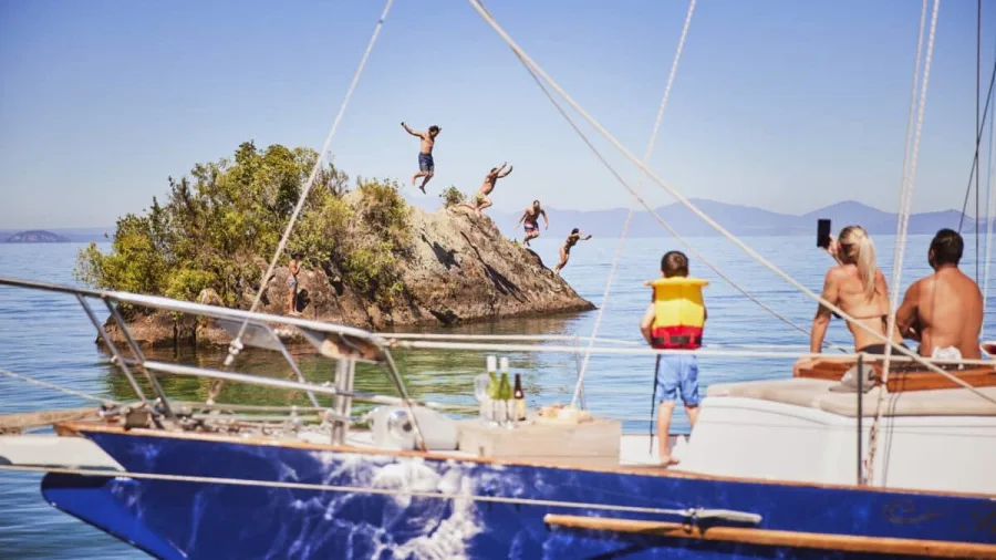 People leap off a rocky islet in Mine Bay as others watch from a yacht on Lake Taupō.