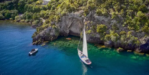 Sailboat and kayakers near the Mine Bay Māori Rock Carvings on Lake Taupō