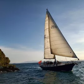Kindred Spirit yacht sailing past cliffs on Lake Taupō during sunset