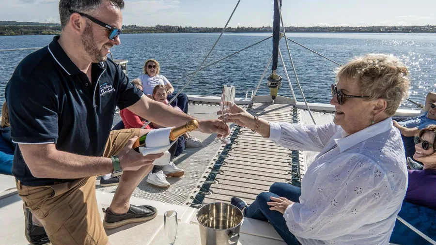 Crew member serving champagne to a guest on board the Tiua catamaran on Lake Taupō