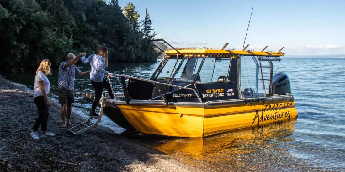 People stepping off a yellow boat onto a quiet lakeside beach at Lake Taupō