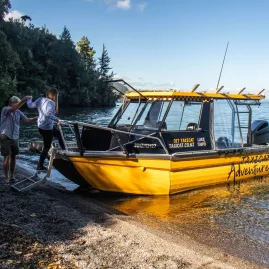 People stepping off a yellow boat onto a quiet lakeside beach at Lake Taupō