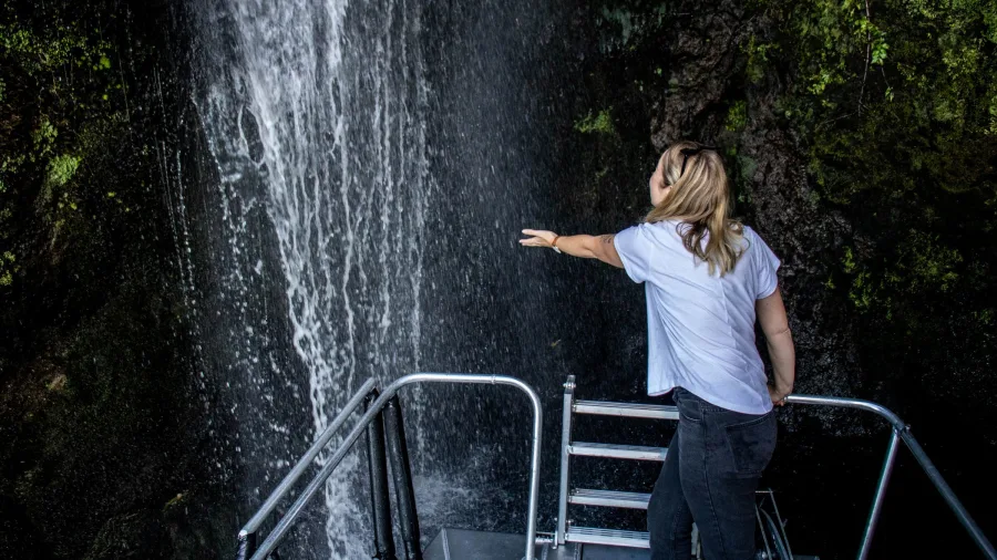 Woman reaching out to touch a waterfall from a boat deck in Taupō