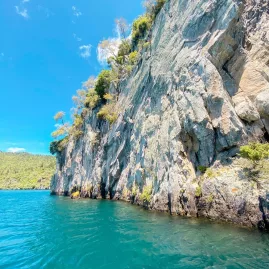 View of towering lakeside cliffs rising from the turquoise water of Lake Taupō under a clear blue sky