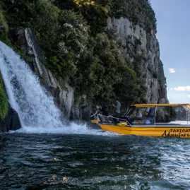 Yellow boat close to a powerful waterfall surrounded by cliffs and native bush in Lake Taupō