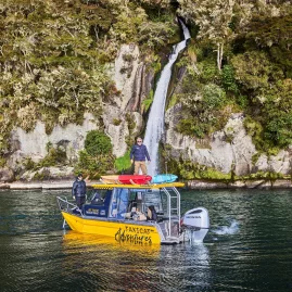 Yellow Taxicat boat floating near a lakeside waterfall with people standing on board in Taupō