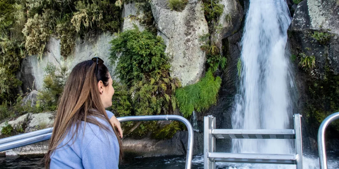 Woman on a boat admiring a small waterfall cascading down rocks into Lake Taupō