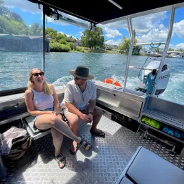 Two passengers seated and chatting on the Taxicat boat during a lake tour in Waitomo