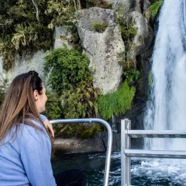Woman on a boat admiring a small waterfall cascading down rocks into Lake Taupō