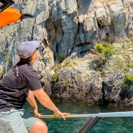 Man on a boat approaching a steep rock face over clear green water during a Taupo tour