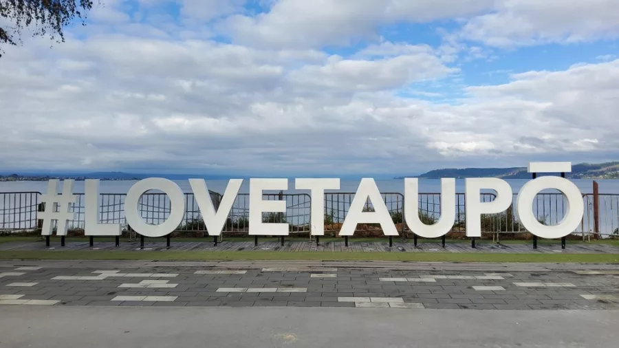 #LOVETAUPŌ sign on the lakefront with Lake Taupō and Tongariro National Park in the background