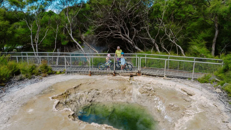 Family with bicycles stops to view a steaming geothermal pool along the Supervolcanic Cycle Trail in Turangi, New Zealand.