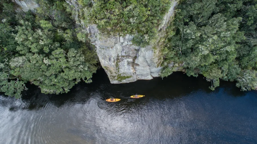 Aerial view of two kayakers paddling along the Kuratau River beside forested cliffs at the southern end of Lake Taupō, New Zealand.