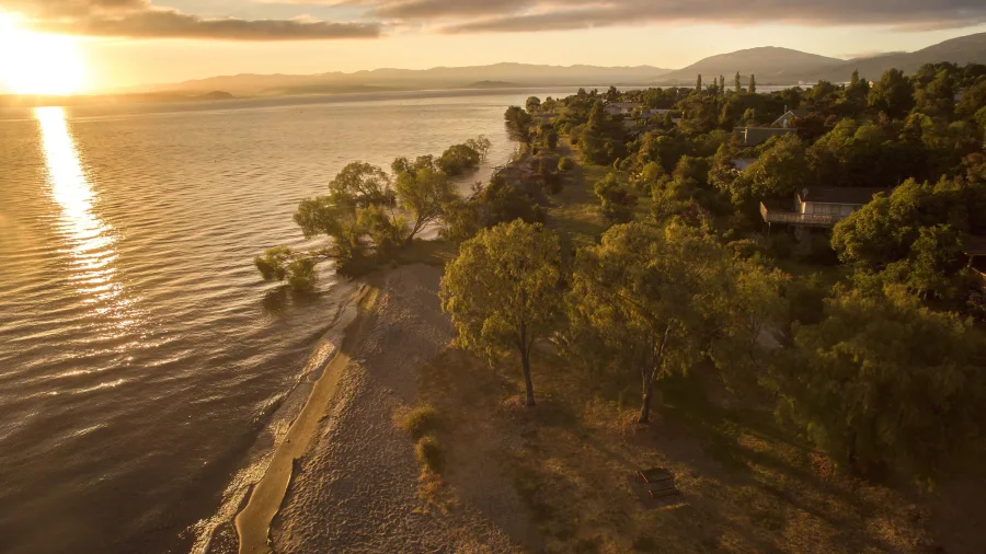 Aerial view of Kuratau’s shoreline at dawn with golden light reflecting over Lake Taupō, New Zealand.