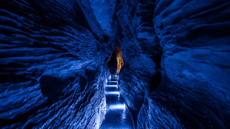 Narrow illuminated passage inside Ruakuri Cave with textured limestone walls