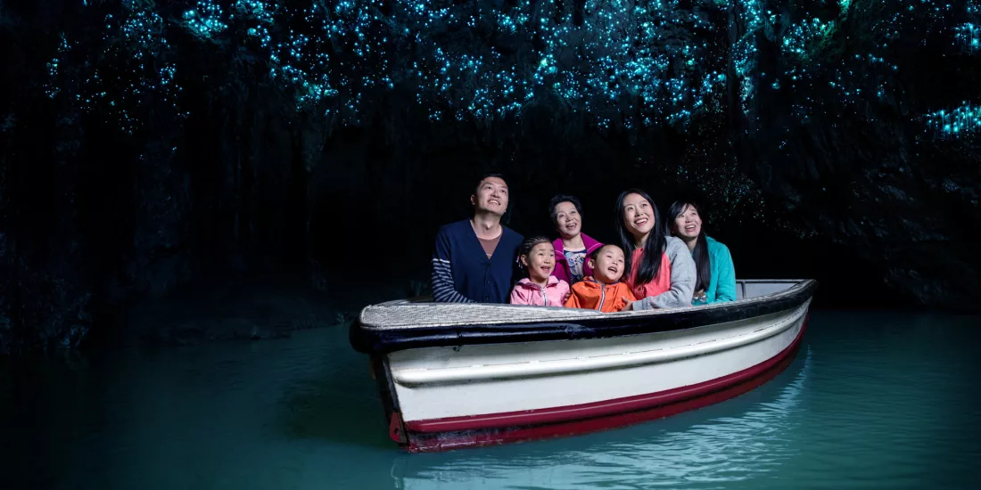 Family on a boat gliding through the Waitomo Glowworm Caves, lit by thousands of tiny blue glowworms overhead