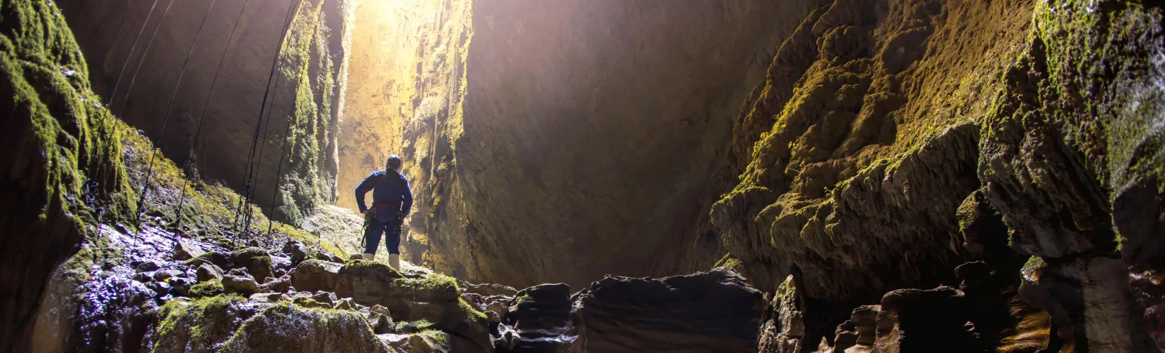 Explorer standing above flowing water inside the Lost World cave in Waitomo surrounded by limestone formations