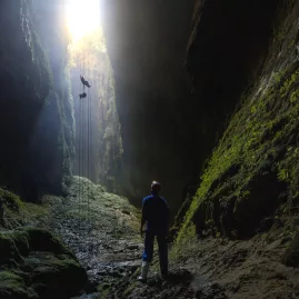Adventure seeker abseiling into the Lost World cave in Waitomo with light streaming from above