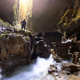 Explorer standing above flowing water inside the Lost World cave in Waitomo surrounded by limestone formations