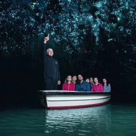 Visitors on a silent boat ride through the Waitomo Glowworm Caves with a guide pointing to the glowing cave ceiling