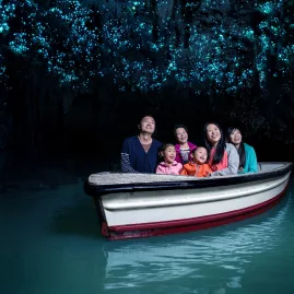 Family on a boat gliding through the Waitomo Glowworm Caves, lit by thousands of tiny blue glowworms overhead