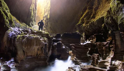 Explorer standing above flowing water inside the Lost World cave in Waitomo surrounded by limestone formations