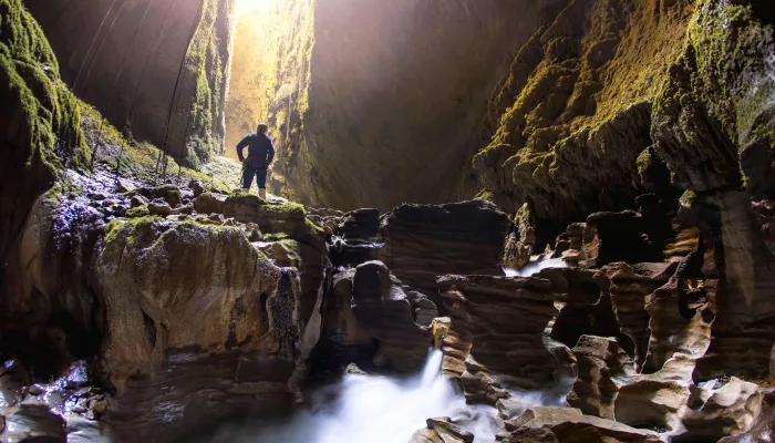 Explorer standing above flowing water inside the Lost World cave in Waitomo surrounded by limestone formations