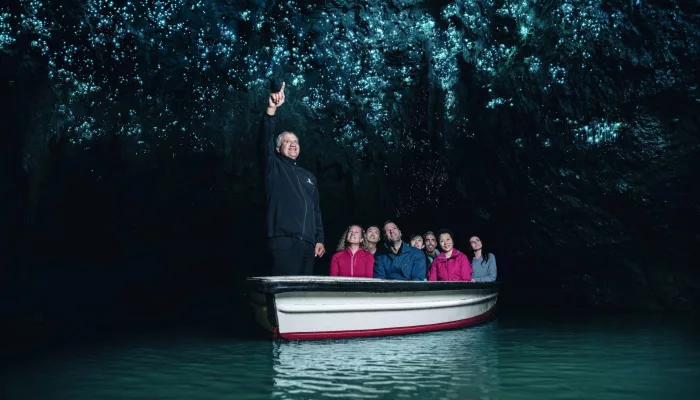 Visitors on a silent boat ride through the Waitomo Glowworm Caves with a guide pointing to the glowing cave ceiling
