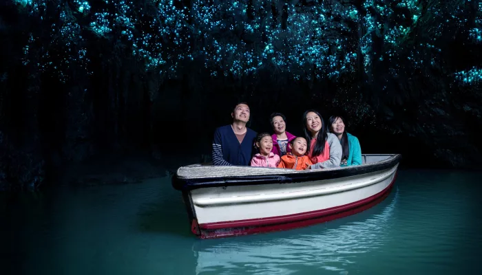 Family on a boat gliding through the Waitomo Glowworm Caves, lit by thousands of tiny blue glowworms overhead