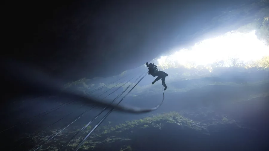 Person abseiling into the Lost World cave in Waitomo with light streaming from the surface above