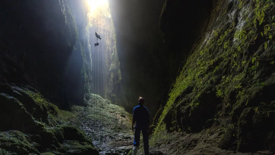 Adventure seeker abseiling into the Lost World cave in Waitomo with light streaming from above
