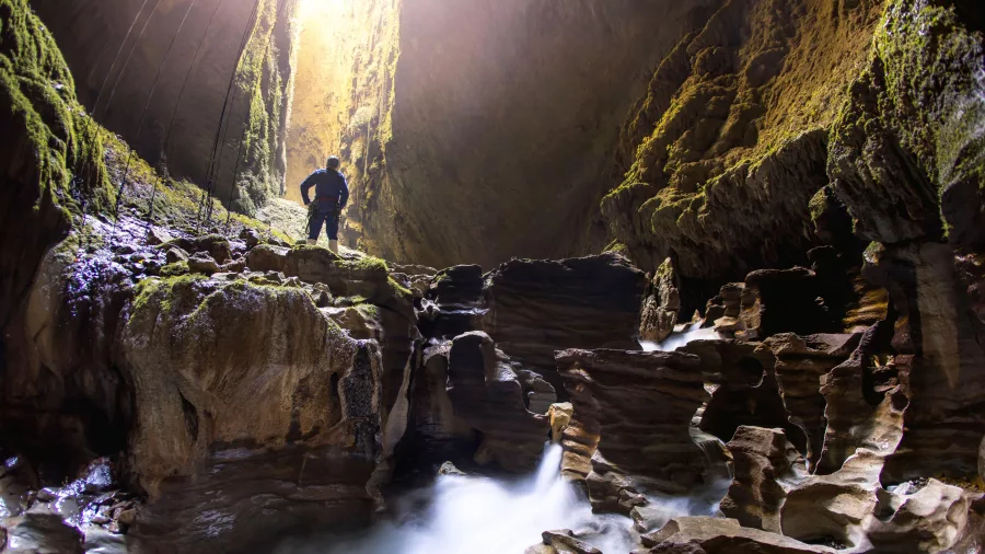 Explorer standing above flowing water inside the Lost World cave in Waitomo surrounded by limestone formations