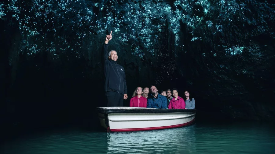 Visitors on a silent boat ride through the Waitomo Glowworm Caves with a guide pointing to the glowing cave ceiling