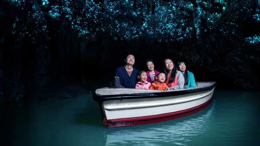Family on a boat gliding through the Waitomo Glowworm Caves, lit by thousands of tiny blue glowworms overhead