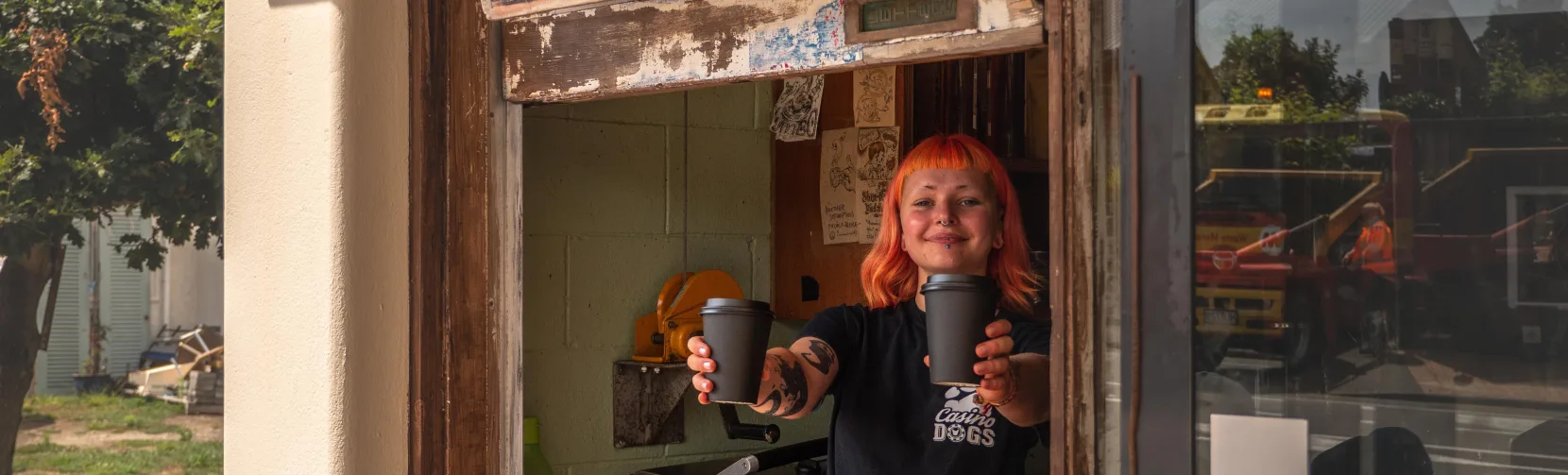 Barista serving takeaway coffee at the window of Raumati Social Club on the Kapiti Coast, New Zealand