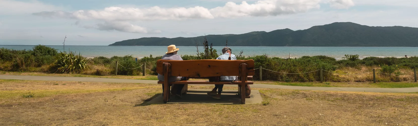 Two people sitting on a bench overlooking Kapiti Island from Paraparaumu Beach, Kapiti Coast, New Zealand