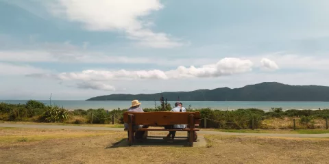 Two people sitting on a bench overlooking Kapiti Island from Paraparaumu Beach, Kapiti Coast, New Zealand