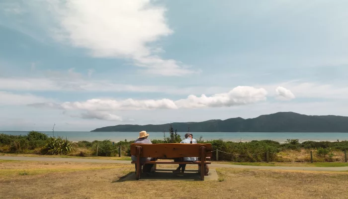 Two people sitting on a bench overlooking Kapiti Island from Paraparaumu Beach, Kapiti Coast, New Zealand