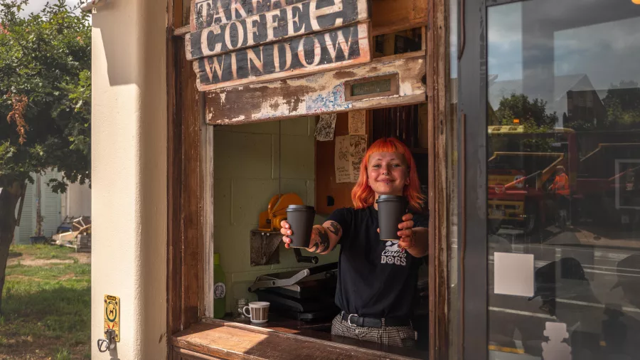 Barista serving takeaway coffee at the window of Raumati Social Club on the Kapiti Coast, New Zealand