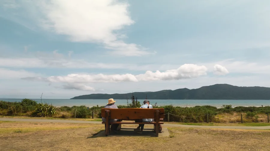 Two people sitting on a bench overlooking Kapiti Island from Paraparaumu Beach, Kapiti Coast, New Zealand