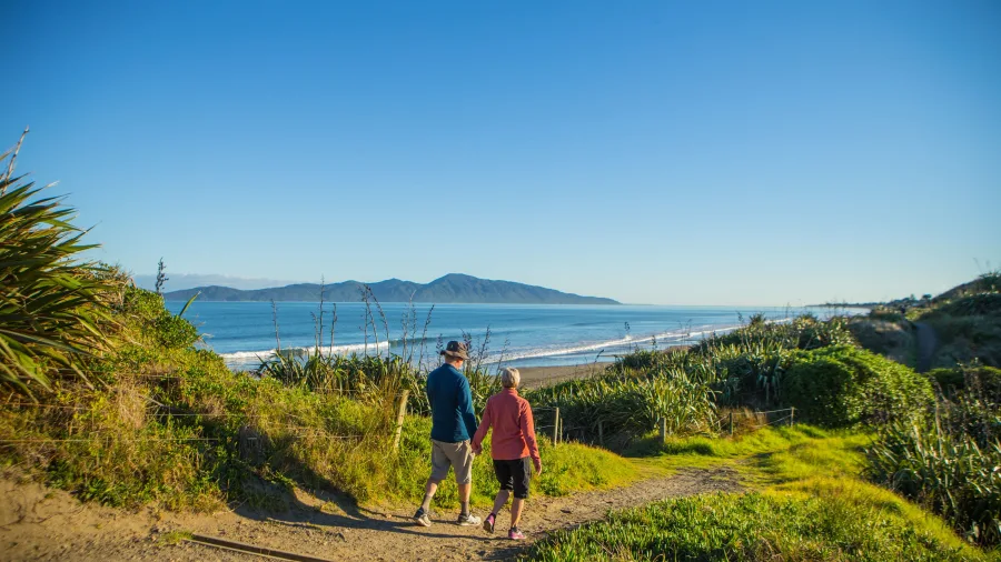 Couple walking down a coastal track at Queen Elizabeth Park with Kapiti Island in the distance, Paraparaumu Beach, New Zealand