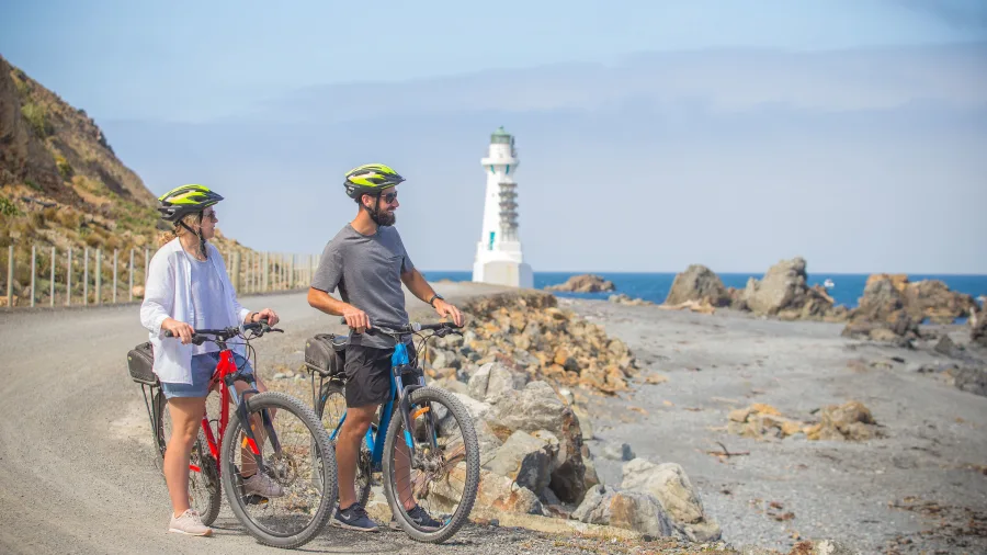 Cyclists riding along Pencarrow Coast Road with Pencarrow Lighthouse in the background, Eastbourne, Lower Hutt, New Zealand