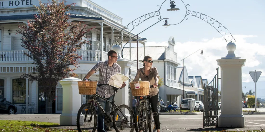 Couple cycling through Martinborough town square with map
