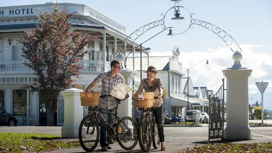 Couple cycling through Martinborough town square with map