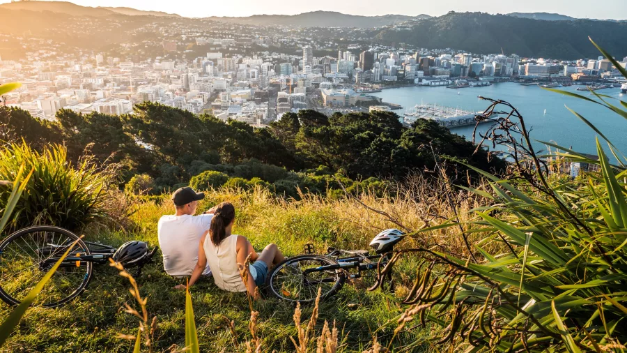 Couple with bikes relaxing at Mount Victoria Lookout overlooking Wellington city and harbour at sunset
