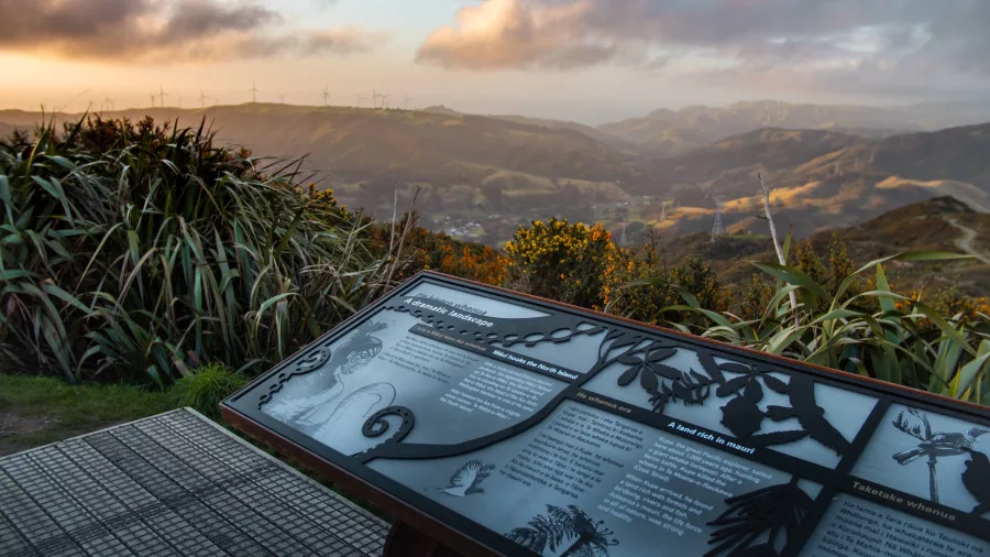 Interpretive panel at Makara Peak with distant view of wind turbines and rolling hills near Wellington at sunset