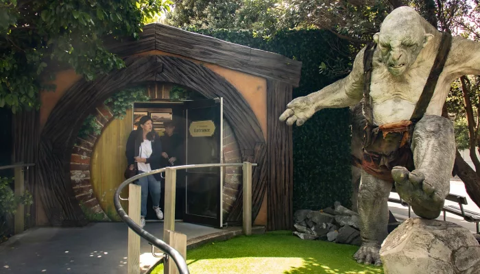 Visitors exiting through hobbit-style door at Wētā Workshop with troll sculpture beside them