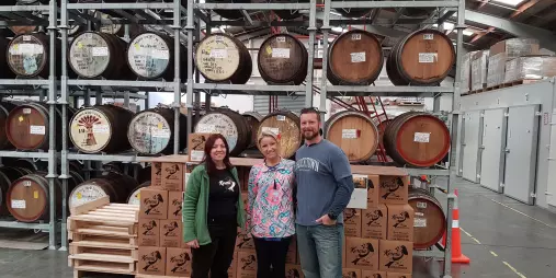 Guests standing in front of stacked oak barrels and cartons at Kereru Brewing during a craft beer tour