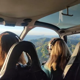 Two women wearing headsets inside a helicopter flying over Wellington’s coastal wind farm