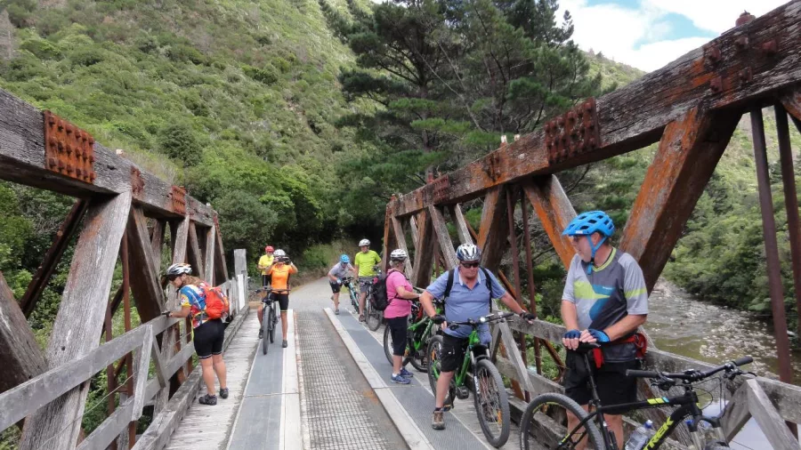Cyclists crossing a historic bridge on a scenic trail through a wooded valley